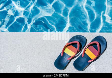 vue de dessus des tongs sur le bord blanc d'une piscine avec de l'eau bleuâtre en arrière-plan. concept de vacances d'été lgbt. diversité. fierté. Banque D'Images