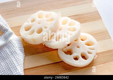 Des tranches de racine de lotus blanc (renkon) sur la planche à découper en bois dans la cuisine de près. Banque D'Images