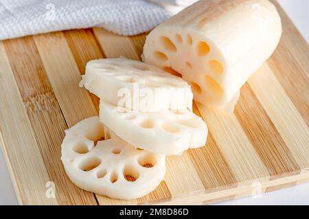 Des tranches de racine de lotus blanc (renkon) sur la planche à découper en bois dans la cuisine de près. Banque D'Images