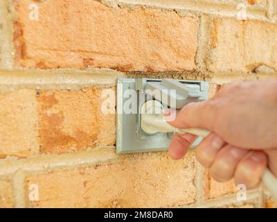 Homme branchant un cordon d'alimentation, puis débranchez-le d'une prise électrique extérieure. Deux prises d'alimentation extérieures couvertes sur un mur en briques. Banque D'Images