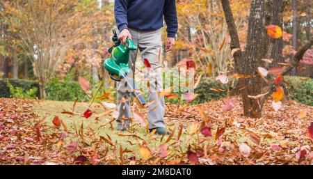 Homme utilisant un souffleur électrique pour souffler les feuilles d'automne de la pelouse. Un travailleur du paysage débarque les feuilles de chute de la cour résidentielle. Banque D'Images