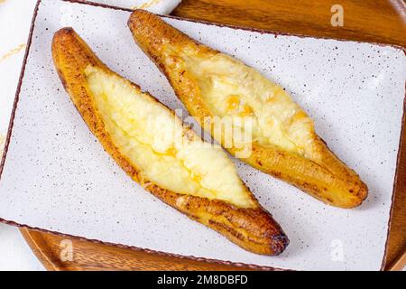 Vue de dessus des plantains mûrs cuits au fromage (Plantain Canoe ou Platanos Asados con Queso) sur une assiette sur fond de bois. Banque D'Images