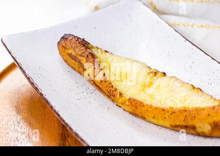 Plantains mûrs cuits au fromage (Plantain Canoe ou Platanos Asados con Queso) sur une assiette sur fond de bois. Banque D'Images