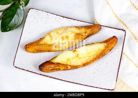 Vue de dessus des plantains mûrs cuits au fromage (Plantain Canoe ou Platanos Asados con Queso) sur une assiette sur fond de bois. Banque D'Images