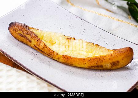 Plantains mûrs cuits au fromage (Plantain Canoe ou Platanos Asados con Queso) sur une assiette sur fond de bois. Banque D'Images