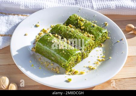 Traditionnelle asiatique douce pistache baklava ou pahlava avec noix et sirop sur une assiette blanche sur fond de bois clair. Banque D'Images