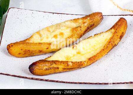 Plantains mûrs cuits au fromage (Plantain Canoe ou Platanos Asados con Queso) sur une assiette sur fond de bois. Banque D'Images