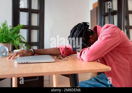 Épuisé homme africain surchargé travailleur à distance dormant sur le bureau, souffrant de l'épuisement indépendant Banque D'Images