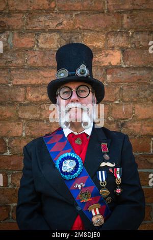 Portrait d'un ancien homme distingué steampunk portant un chapeau avec des lunettes attachées et un costume de cérémonie . Il a une magnifique barbe mauviée. Banque D'Images