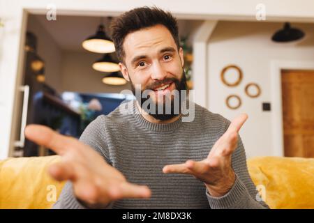 Portrait d'un jeune homme barbu souriant, en train de gesturer tout en étant assis sur un canapé dans la salle de séjour Banque D'Images