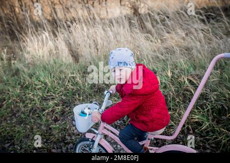 Une petite fille sur un vélo roule sur une route de terre. Un enfant ukrainien immigrant reçoit un don de vélo d'occasion d'une famille d'accueil. le petit enfant apprend r Banque D'Images