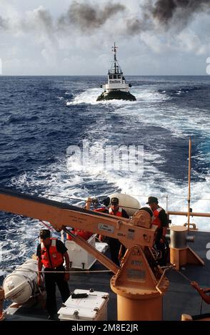 Un remorqueur commercial suit le grand patrouilleur USCGC KISKA (WPB-1336) de la Garde côtière, tandis que des membres de l'équipage à bord du KISKA utilisent une grue pour abaisser un bateau dans l'eau pendant l'opération Steel Box. Le KISKA est en place pour assurer la sécurité lors de la livraison de munitions chimiques à l'atoll Johnston. Objet opération/série : CAISSE EN ACIER pays : Océan Pacifique (POC) Banque D'Images