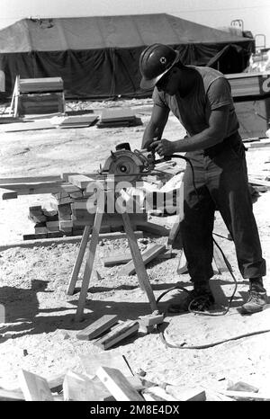 Un Seabee du bataillon de construction mobile navale 40 (NMCB-40) coupe des blocs de bois pendant qu'il aide à construire des cadres de tente pendant l'opération Desert Shield. Objet opération/série : BOUCLIER DU DÉSERT pays : Arabie saoudite (SAU) Banque D'Images