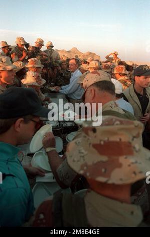 Le président George Bush tient sa plaque alors qu'il passe par une ligne de mess lors d'une visite de Thanksgiving dans un campement du désert. Mme Bush accompagne son mari, le président George Bush, lors d'une série de visites aux troupes américaines qui se trouvent en Arabie saoudite pour l'opération Desert Shield. Objet opération/série : BOUCLIER DU DÉSERT pays : Arabie saoudite (SAU) Banque D'Images