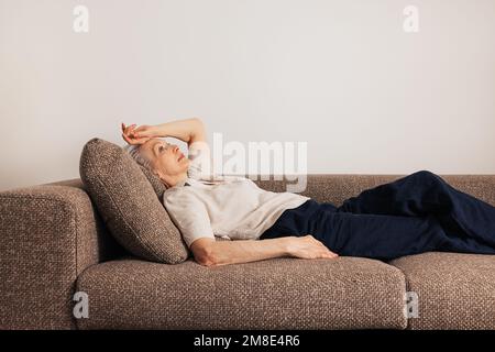 Femme âgée et fatiguée, couchée sur un lit. Une femme âgée se sent malade. Banque D'Images