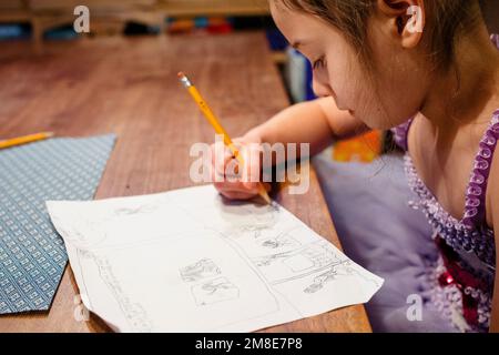 Une petite fille sis à la table en costume soigneusement dessiner une bande dessinée Banque D'Images