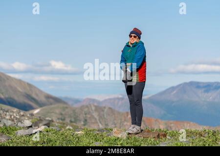 Femme debout dans une région alpine du nord du Canada pendant l'été. Porter des vêtements de randonnée avec de vastes montagnes en arrière-plan. Banque D'Images