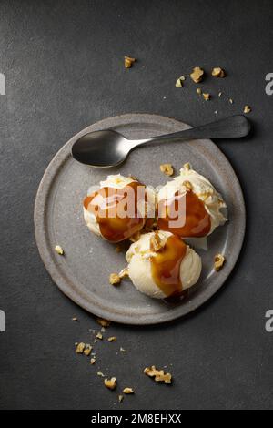 assiette de glace à la vanille avec sauce caramel et noix sur fond gris foncé, vue du dessus Banque D'Images