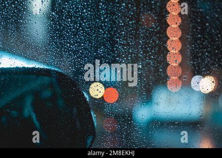 Gouttes de pluie sur le pare-brise de la voiture pendant la conduite de nuit lors d'une soirée pluvieuse Banque D'Images