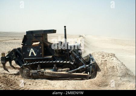 Un membre de Co. A, 299th Engineer BN., attaché au 3rd Engineer BN., 24th Infantry Division, a enfreint une berme menant en Iraq à l'aide d'un tracteur de terrassement blindé D-7G pendant l'opération Desert Storm. Objet opération/série : TEMPÊTE DANS LE DÉSERT pays : Arabie saoudite (SAU) Banque D'Images