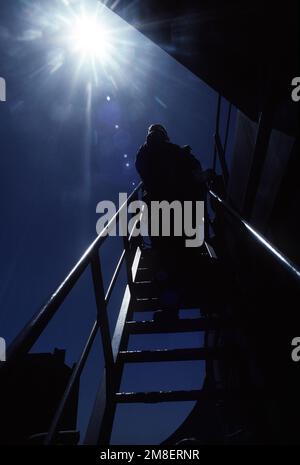 Un membre du détachement de la Marine du porte-avions à propulsion nucléaire USS THEODORE ROOSEVELT (CVN-71) est silhoueté par le soleil lorsqu'il avance sur une échelle lors de l'entraînement de l'équipe d'embarquement à bord du lubrificateur USNS JOSHUA HUMPRHEYS (T-AO-188). Les Marines sont formées par des membres de l'équipe Sea-Air-Land (SEAL) 8, qui a fourni des équipes d'embarquement pour aider à l'application des sanctions commerciales de l'ONU contre l'Iraq pendant l'opération Desert Storm. Sujet opération/série: TEMPÊTE DANS LE DÉSERT pays: Mer Rouge Banque D'Images