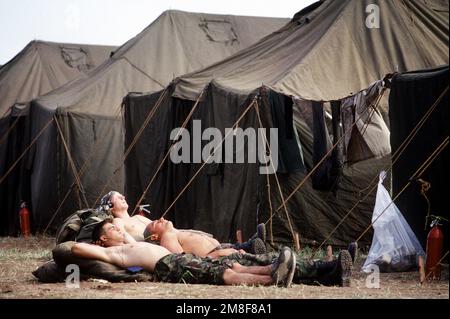 Trois militaires hors service se détendent au soleil entre deux rangées de tentes à la base de soutien des services humanitaires établie pour l'opération fournir confort, un effort multinational pour aider les réfugiés kurdes dans le nord de l'Irak et le sud de la Turquie. Sujet opération/série: FOURNIR LE CONFORT base: Silopi pays: Turquie (TUR) Banque D'Images