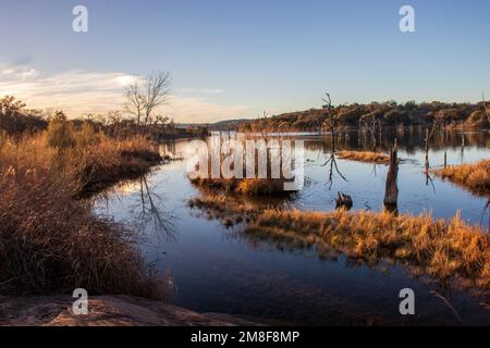 Le coucher du soleil projette une lumière d'une heure dorée sur le lac, créant des ombres et des reflets en automne. Parc national du lac d'encres Burnet, Texas. Banque D'Images