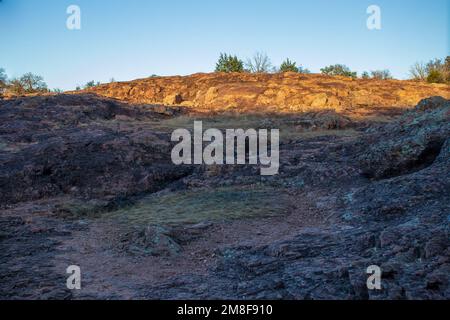 Le sentier de randonnée de Texas Hill Country monte en haut d'un sentier en pierre de granit, tandis que la lumière du soleil illumine la falaise. Parc national du lac d'encres Burnet, Texas. Banque D'Images