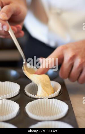 Ma pâtisserie est mon art. Gros plan d'un boulanger poussant la pâte à gâteau d'une cuillère dans une plaque de cuisson Banque D'Images