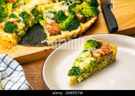 Vue panoramique de délicieux brocoli et quiche de saumon maison fraîchement cuits sur une planche à découper en bois et une tranche de plat en céramique brune sur une patte en bois Banque D'Images