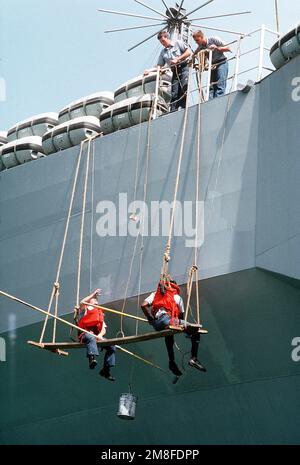 Un marin à bord du navire de commandement amphibie USS BLUE RIDGE (LCC-19) abaisse un soda à un autre membre de l'équipage. Les marins de l'échafaudage peignent la coque du navire alors qu'il est assis dans le port après son arrivée de la région du golfe Persique où il a été déployé pendant les opérations Bouclier du désert/tempête du désert. Objet opération/série : BOUCLIER DU DÉSERT TEMPÊTE DU DÉSERT pays : Bahreïn (BHR) Banque D'Images