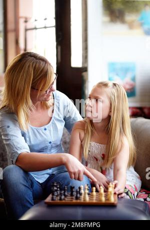 Envisager la prochaine étape. Une jeune fille blonde envisage sa prochaine étape en jouant aux échecs avec sa mère. Banque D'Images