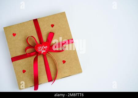 Un cadeau enveloppé dans une boîte kraft avec un ruban de satin rouge a été isolé sur du blanc. Le concept d'un cadeau, nouvel an, Saint-Valentin, anniversaire, salutations Banque D'Images