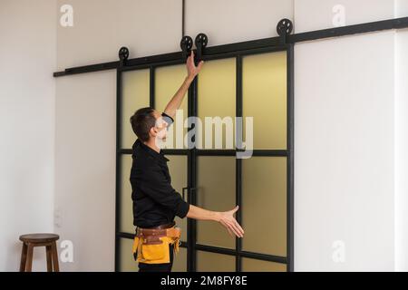 hommes ouvriers charpentiers installant une porte intérieure en verre avec un cadre en bois dans un nouvel appartement de luxe. Banque D'Images