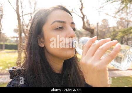 Gros plan portrait de la tête d'une femme qui boit de l'eau. Femme tenant une bouteille en verre debout à l'extérieur. Les boissons de fille sont toujours propres aqua pour le régime, les soins de la peau Banque D'Images