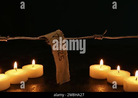 Numéro de prisonnier, barbelés et bougies allumées sur fond sombre. Journée internationale de commémoration de l'Holocauste Banque D'Images