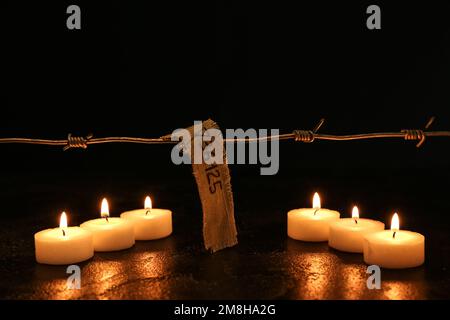 Numéro de prisonnier, barbelés et bougies allumées sur fond sombre. Journée internationale de commémoration de l'Holocauste Banque D'Images
