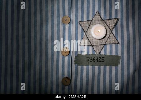 Bougie en feu, insigne juif et numéro sur l'uniforme de prisonnier, gros plan. Journée internationale de commémoration de l'Holocauste Banque D'Images