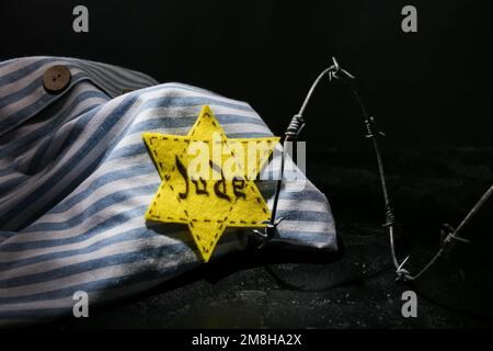 Uniforme de prisonnier, badge juif et barbelé sur fond sombre. Journée internationale de commémoration de l'Holocauste Banque D'Images