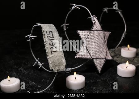 Numéro de prisonnier, badge juif, barbelés et bougies allumées sur fond noir. Journée internationale de commémoration de l'Holocauste Banque D'Images