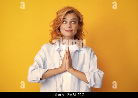 Portrait de la femme heureuse souriant et disant la prière. Jolie fille jouit d'une atmosphère paisible, tient les mains dans le geste de prière, isolé sur jaune Banque D'Images