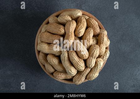 Bol plein de cacahuètes décortiquées sur fond sombre, vue de dessus Banque D'Images