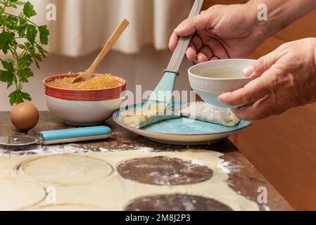 Les mains de l'homme avec un bol et une brosse de cuisine étalant les oeufs battus sur les bonbons de pâte feuilletée avant des mettre dans le four. Banque D'Images