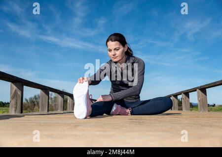 Femme sportive en train de s'asseoir en train de s'étirer exercice d'échauffement avant de courir ou de faire du jogging. Banque D'Images