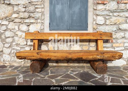 Gros plan d'un banc en bois vide fait de troncs d'arbres en face d'un chalet de montagne (maison en pierre). Trento, Trentin-Haut-Adige, Italie, Europe. Banque D'Images