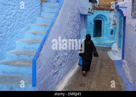 Afrique du Nord. Maroc. Chefchaouen. Une femme maghrebin vêtue de djellaba marchant dans une rue bleue de la médina Banque D'Images