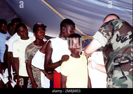 Hôpital Corpsman troisième classe (HM3) Ken Stewart, de l'unité de médecine préventive environnementale de la marine n° 2 (NEPMU-2) Norfolk, va, donne des coups de feu contre le tétanos aux Haïtiens du camp 4 de la base navale. Objet opération/série: BASE DE SIGNAL MARITIME: Guantanamo Bay pays: Cuba (CUB) Banque D'Images