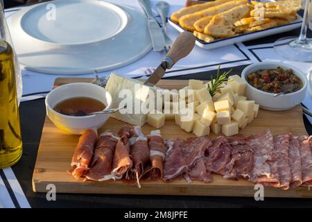 Assortiment de fromages et de viandes transformées sur une assiette en bois dans un restaurant à l'extérieur éclairé par la lumière naturelle, composition réaliste dans un Banque D'Images