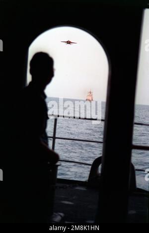 Machiniste Mate First Class (MM1) Jeffrey S. Randell regarde de la queue du porte-avions à propulsion nucellaire USS CARL VINSON (CVN-70) et réfléchit sur la journée. Un F-14 Tomcat est entrant dans la zone d'atterrissage alors que le croiseur de missiles guidé USS ANTIETAM (CG-54) suit la route en position de garde d'avion. Pays: Océan Indien (CIO) Banque D'Images