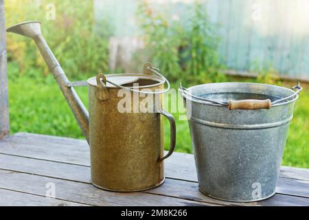 Seau en métal avec eau et arrosoir sur le porche en bois Banque D'Images